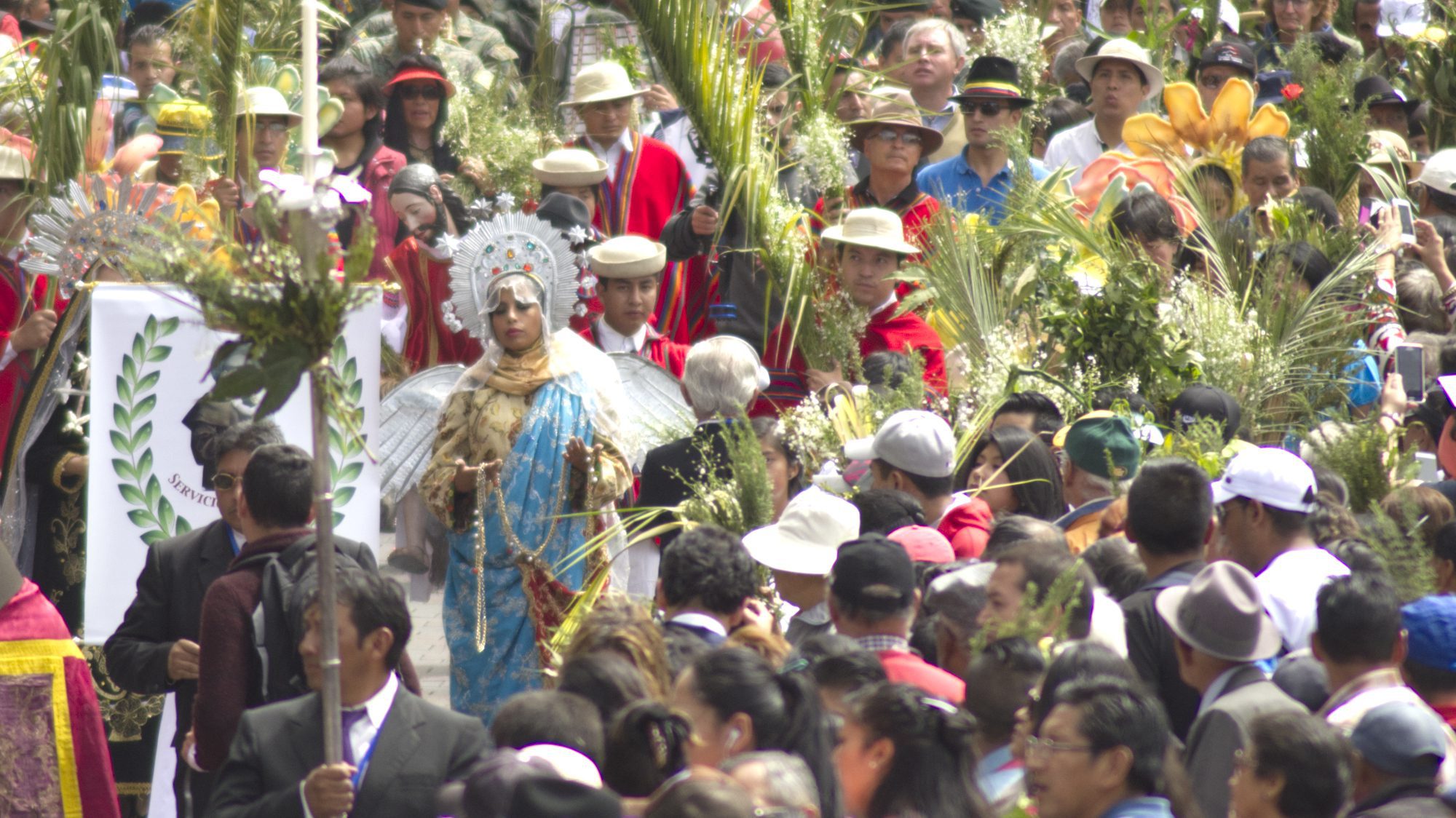 La Virgen de Quito camina por una acera llena de gente con ramos para el Domingo de Ramos