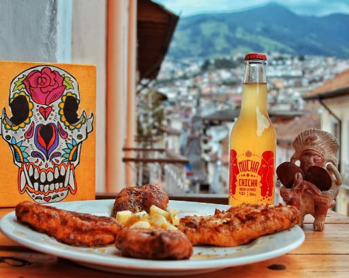 Vista desde Sereno Moreno Primer plano: delicioso plato de comida, botella de chicha y arte ecuatoriano; fondo: vista de Quito.