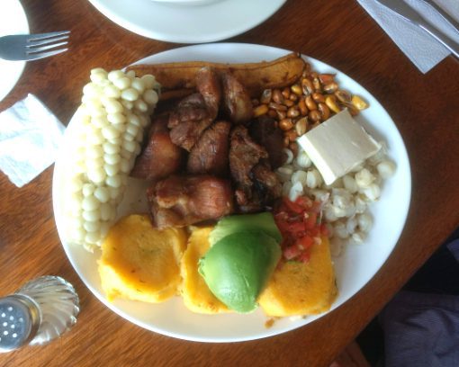 Fritada tradicional Un plato completo de fritada que incluye cerdo frito, hamburguesas de patata, mazorca de maíz, maíz tostado, maíz, queso y aguacate.