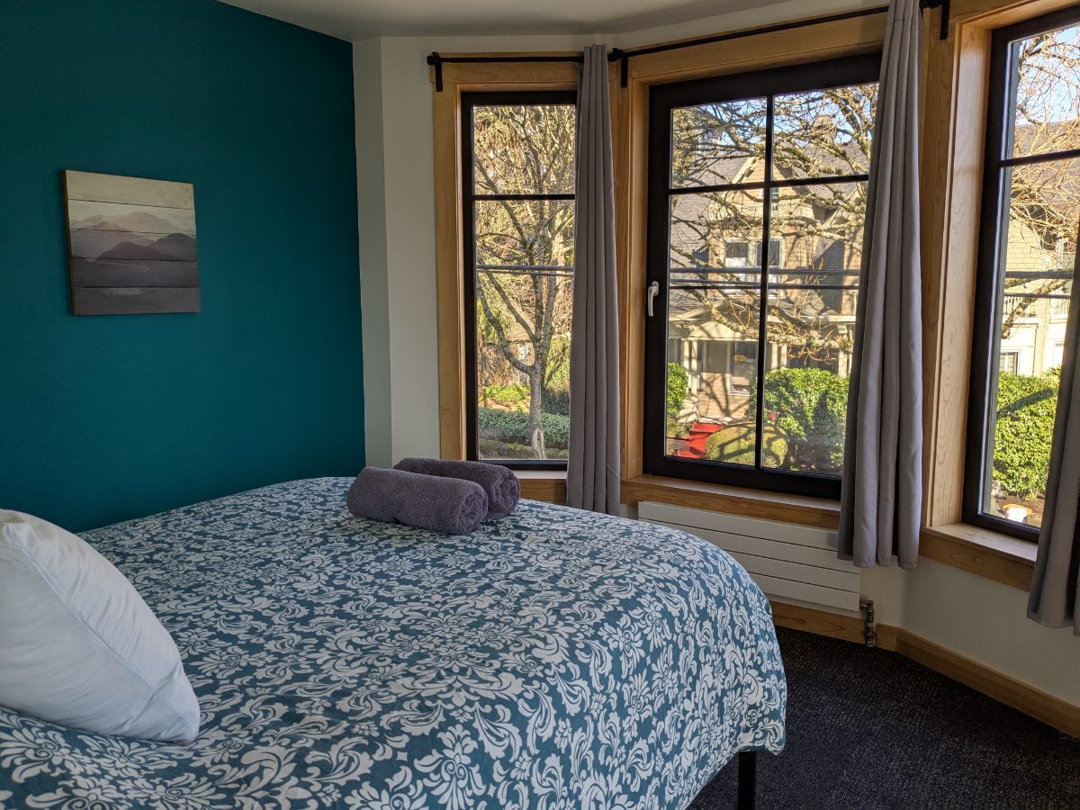 Queen bed looks out through a triple set of windows 