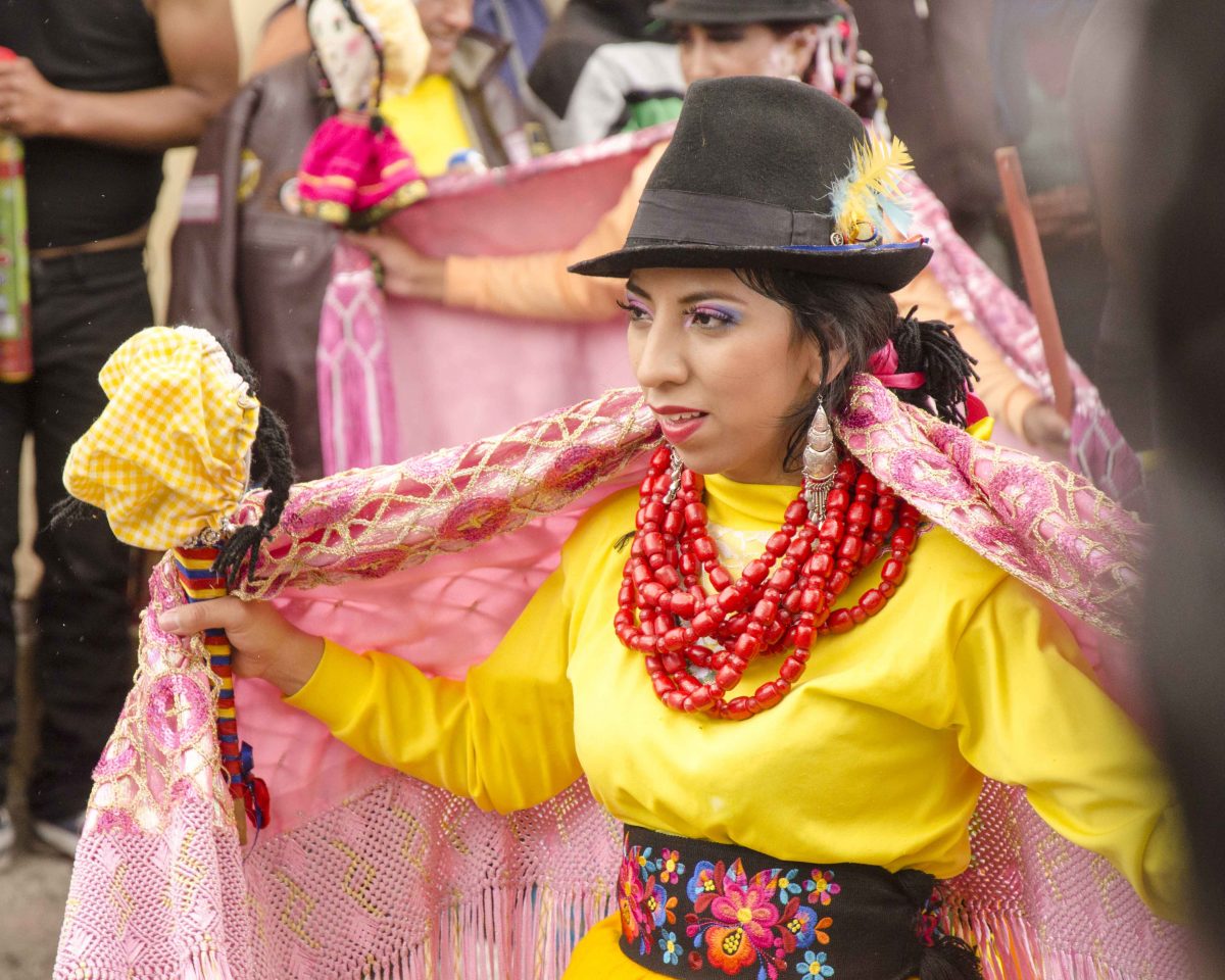 shawl Dancer dressed in bright yellow shirt, pink shawl, and heavy red necklace also wears a dark brown felt hat, Carnaval in Guamote