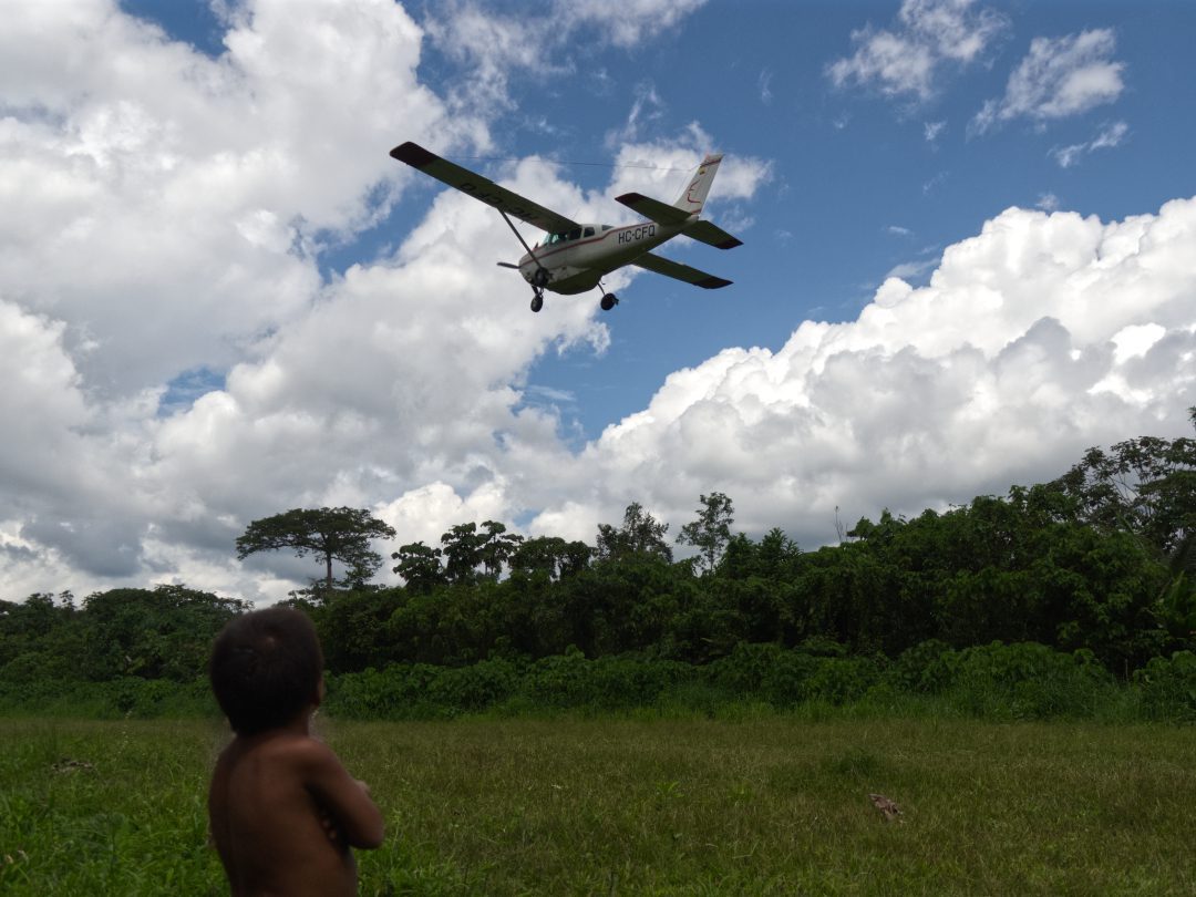 A Waorani child watches as a plane takes off from the grass runway in Toñampare