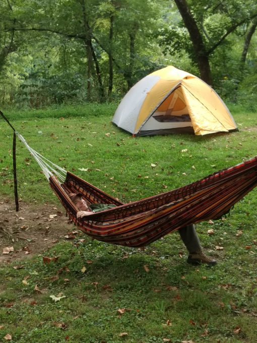 A man in a hammock with an REI 4 person tent in the background.