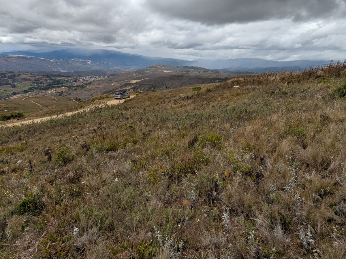 View from a mountainside above the road to Cuemal, Peru, with a car parked on the narrow roadside and the valley stretching out below.