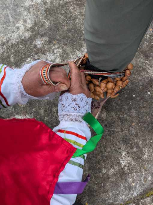 A Cuemal dancer ties a deer toe anklet to the leg of a tourist.