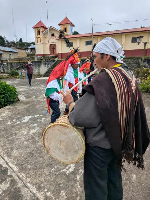A musician places a pipe to his mouth with on hand while beating a drum with another.